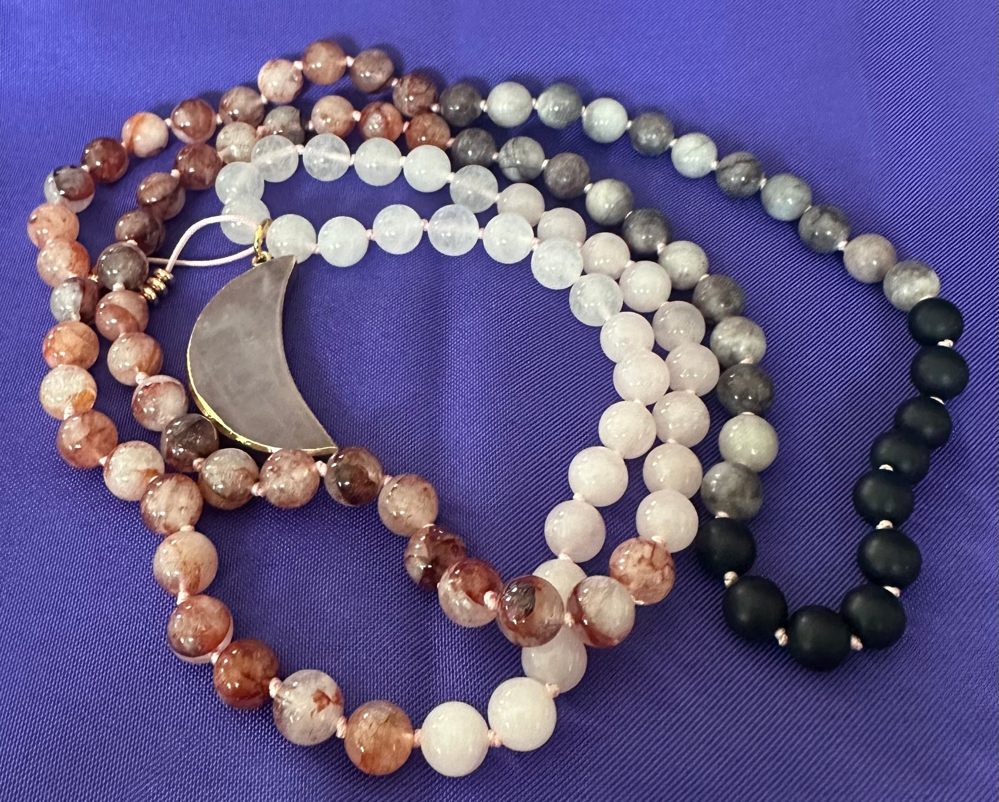 Set of beaded necklaces with a crescent moon pendant on a purple fabric background