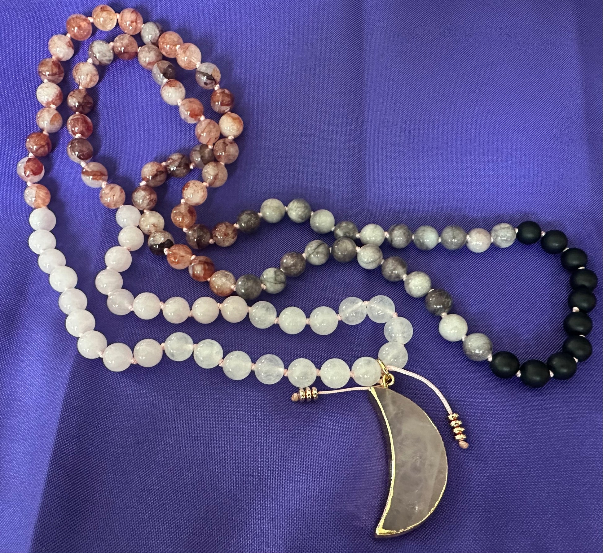 Necklace with multicolored beads and a crescent moon pendant on a purple fabric background
